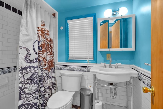 full bath featuring tile walls, a shower with shower curtain, toilet, wainscoting, and a sink