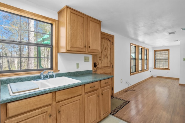 kitchen with a sink, visible vents, baseboards, light wood-style floors, and dark countertops