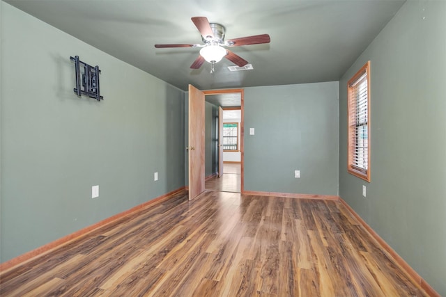 unfurnished room with a ceiling fan, wood finished floors, visible vents, and baseboards