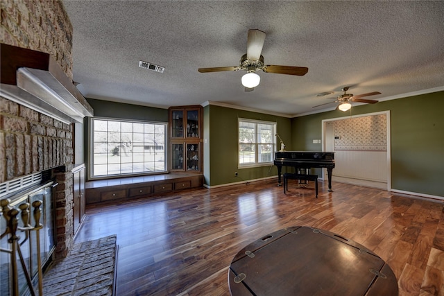 unfurnished living room with ornamental molding, a brick fireplace, visible vents, and wood finished floors