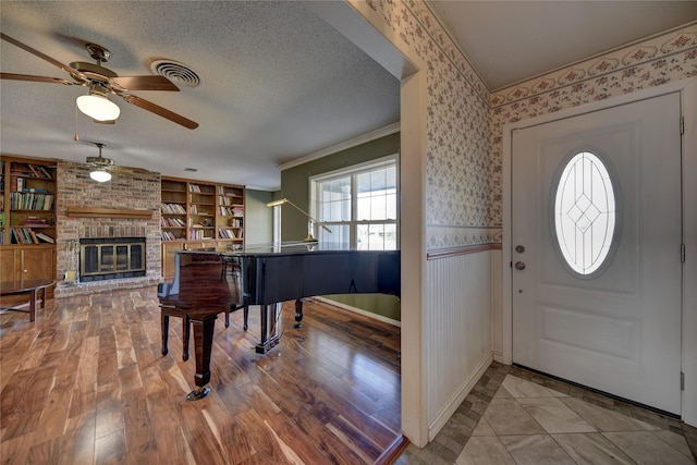 foyer with a textured ceiling, a wainscoted wall, wood finished floors, a brick fireplace, and wallpapered walls