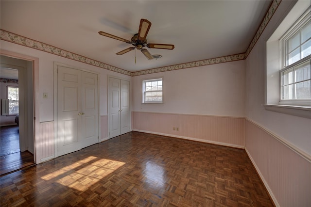 unfurnished bedroom with a ceiling fan, wainscoting, visible vents, and two closets