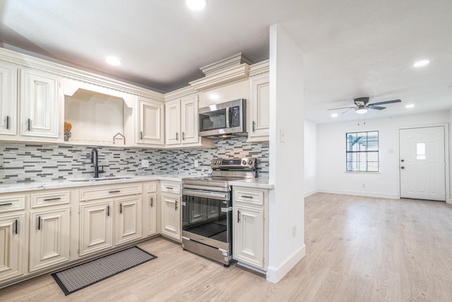 kitchen featuring stainless steel appliances, a sink, light countertops, backsplash, and light wood finished floors