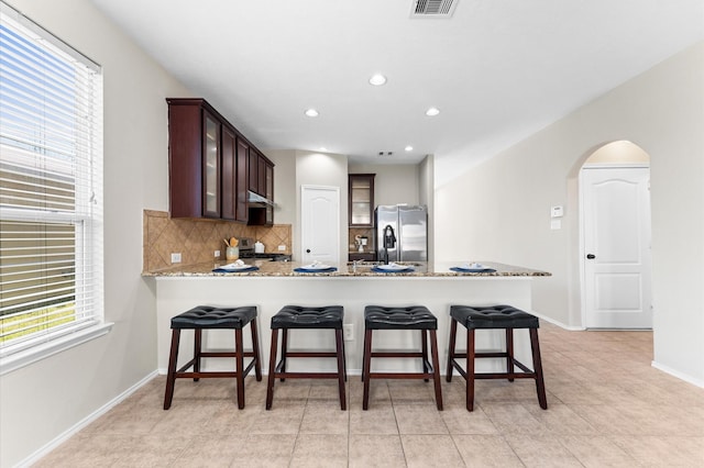 kitchen with arched walkways, backsplash, appliances with stainless steel finishes, glass insert cabinets, and a peninsula