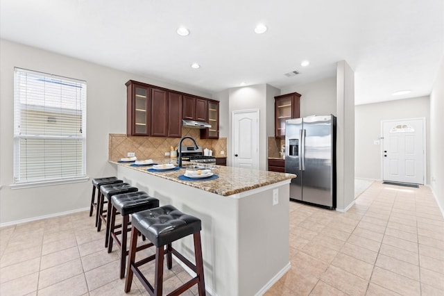 kitchen with decorative backsplash, glass insert cabinets, a peninsula, stainless steel appliances, and under cabinet range hood