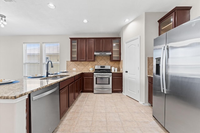 kitchen with under cabinet range hood, a peninsula, a sink, appliances with stainless steel finishes, and tasteful backsplash