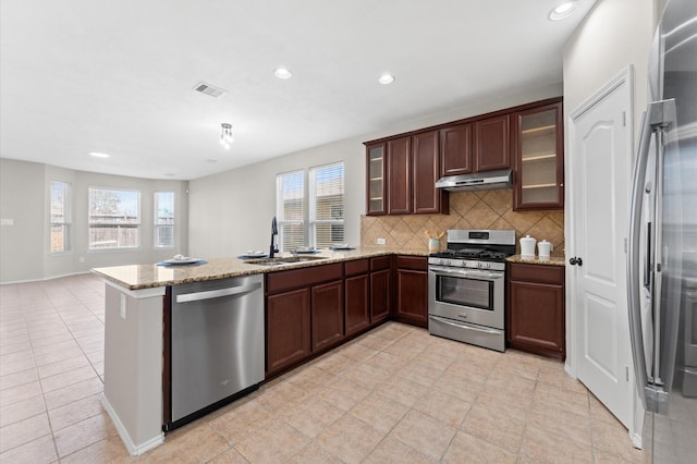 kitchen with under cabinet range hood, stainless steel appliances, a peninsula, a sink, and visible vents