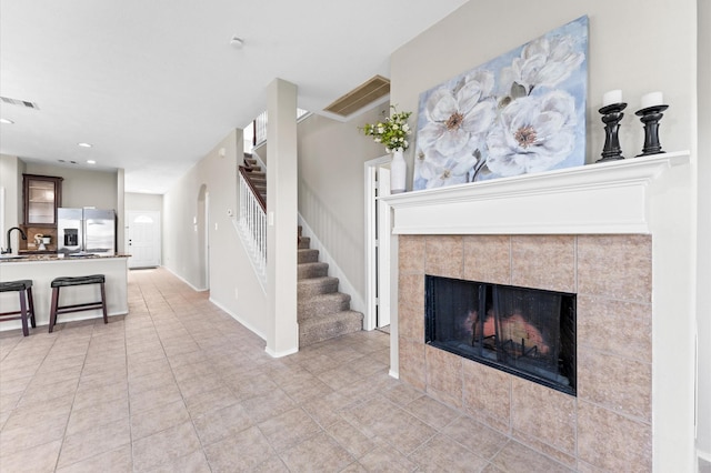 living area featuring visible vents, arched walkways, a tile fireplace, stairs, and recessed lighting