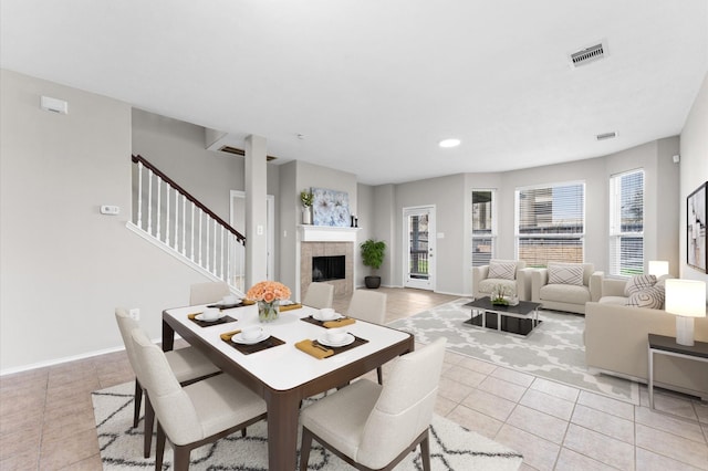 dining room with light tile patterned floors, baseboards, visible vents, a tiled fireplace, and stairway