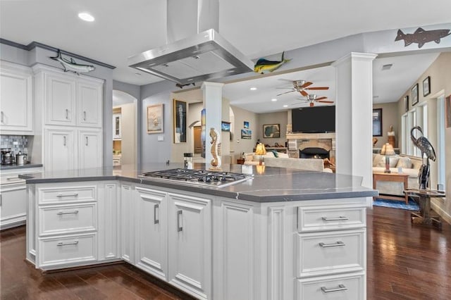 kitchen with arched walkways, open floor plan, dark countertops, island exhaust hood, and stainless steel gas stovetop