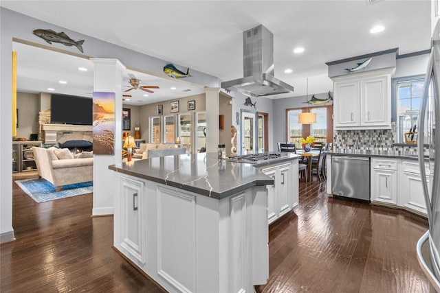 kitchen with decorative columns, dark countertops, appliances with stainless steel finishes, island range hood, and a lit fireplace