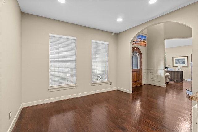 empty room with arched walkways, baseboards, wood finished floors, and recessed lighting