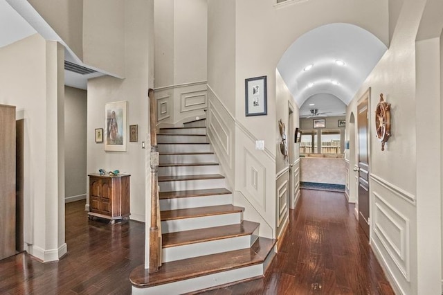 interior space featuring arched walkways, wood-type flooring, lofted ceiling, and a decorative wall