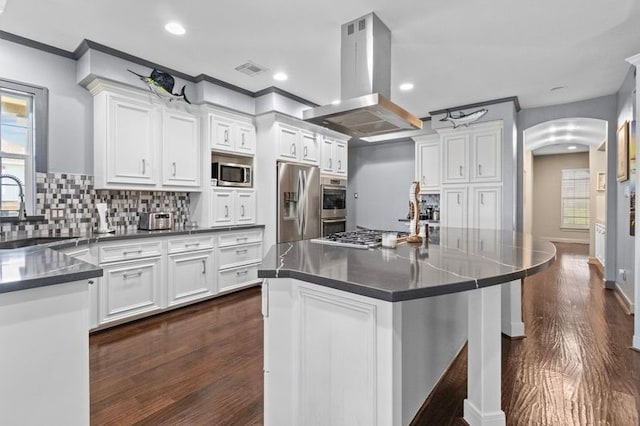 kitchen with stainless steel appliances, dark countertops, a sink, and island range hood