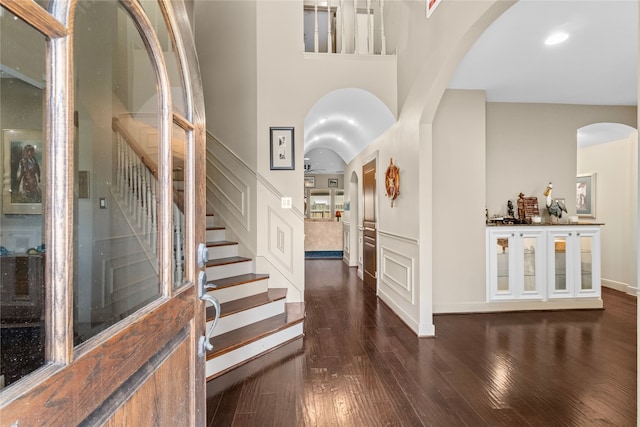 foyer featuring arched walkways, stairway, dark wood-style flooring, a high ceiling, and a decorative wall