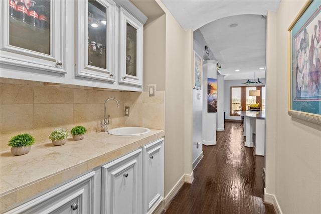 bar featuring arched walkways, dark wood-style flooring, a sink, and baseboards