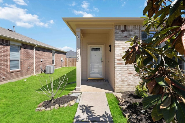 doorway to property featuring cooling unit, brick siding, a yard, and fence