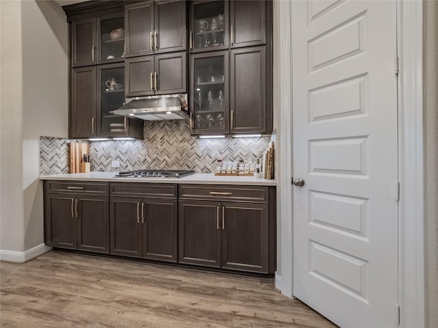 bar with under cabinet range hood, tasteful backsplash, stainless steel gas cooktop, and light wood-style floors