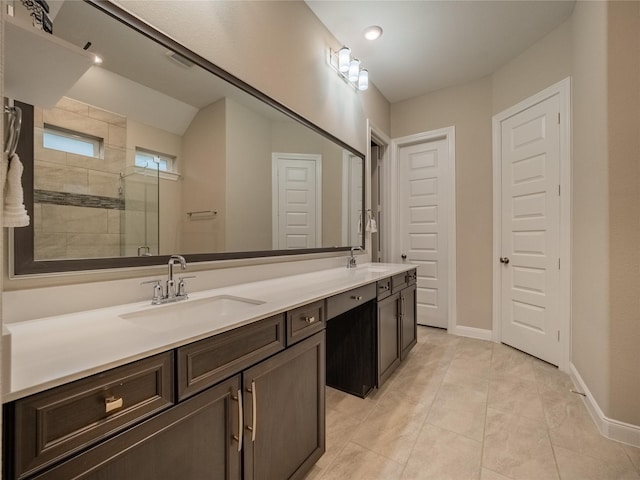 full bath featuring double vanity, baseboards, a tile shower, and a sink