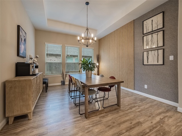 dining room with a tray ceiling, light wood-type flooring, and baseboards