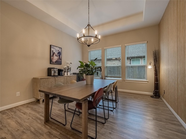 dining room with a notable chandelier, wood finished floors, a raised ceiling, and baseboards