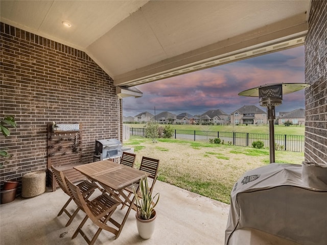 patio terrace at dusk with outdoor dining space, a lawn, area for grilling, and a residential view