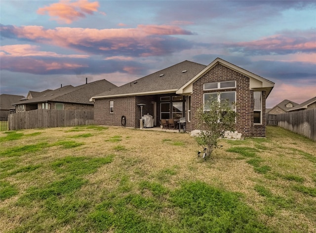 rear view of property featuring a patio, brick siding, a lawn, and a fenced backyard