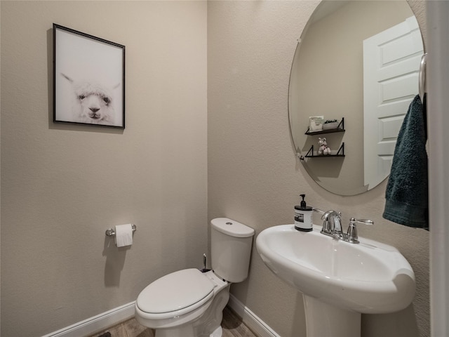 half bath with toilet, baseboards, a sink, and wood finished floors