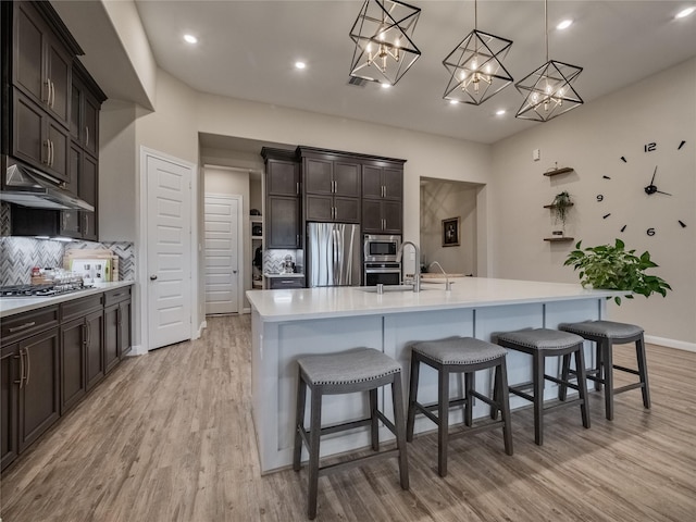 kitchen with tasteful backsplash, stainless steel appliances, light countertops, light wood-style floors, and a sink