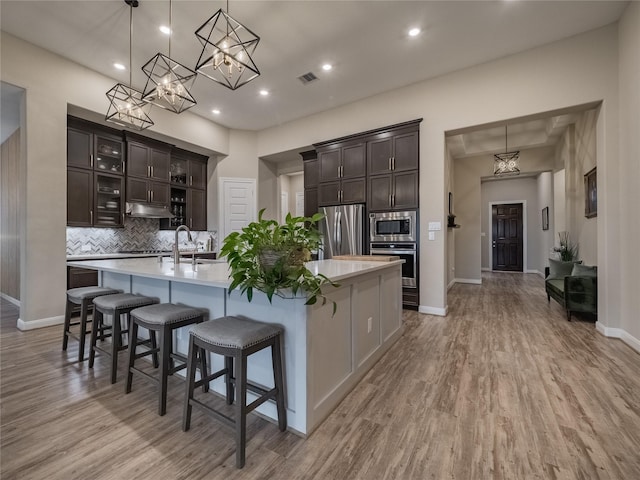 kitchen featuring tasteful backsplash, visible vents, appliances with stainless steel finishes, light wood-style floors, and a large island with sink