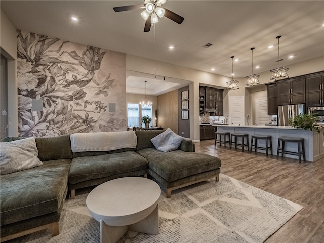 living room featuring ceiling fan with notable chandelier, wood finished floors, and recessed lighting