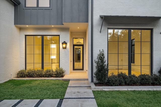 doorway to property featuring a yard, brick siding, and board and batten siding