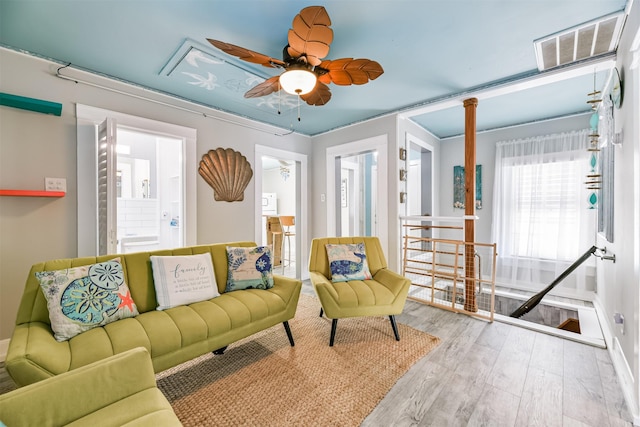 living area with decorative columns, wood finished floors, visible vents, and a ceiling fan