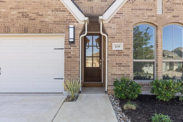 view of exterior entry with a garage and brick siding