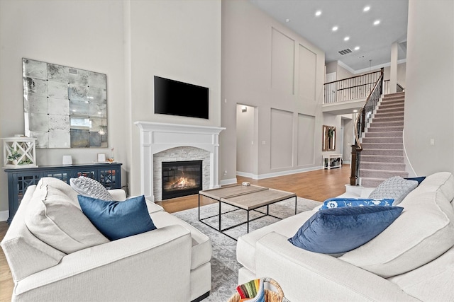 living room featuring visible vents, stairway, wood finished floors, a high ceiling, and a stone fireplace