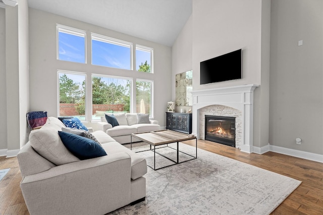 living area with high vaulted ceiling, a fireplace, baseboards, and wood finished floors