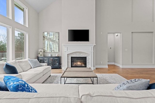 living room featuring high vaulted ceiling, a fireplace, baseboards, and wood finished floors