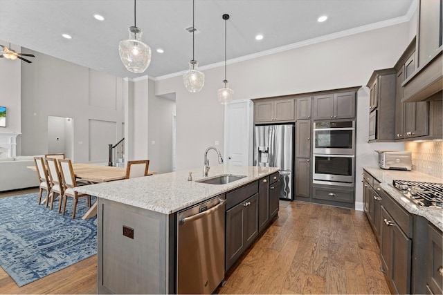 kitchen with light stone counters, appliances with stainless steel finishes, dark wood-style flooring, a kitchen island with sink, and a sink