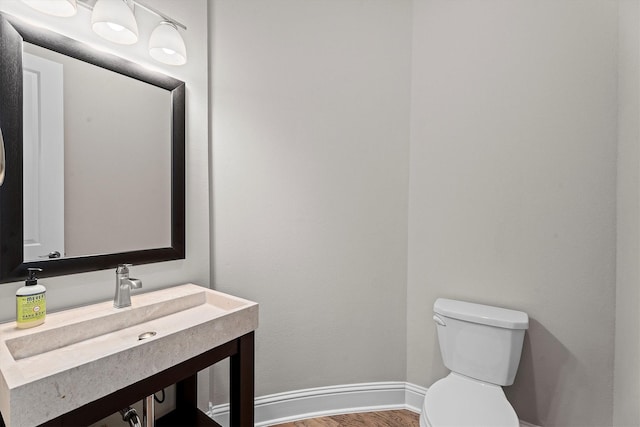 bathroom featuring toilet, baseboards, a sink, and wood finished floors