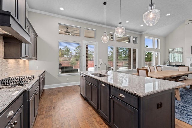 kitchen featuring decorative backsplash, custom range hood, wood finished floors, a kitchen island with sink, and a sink