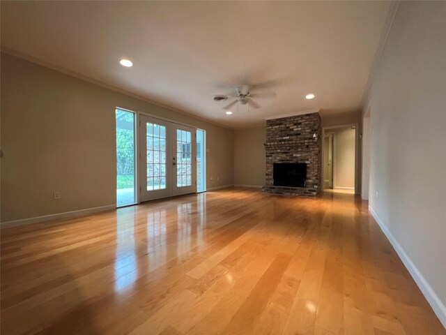 unfurnished living room with a brick fireplace, light wood-style flooring, crown molding, and french doors