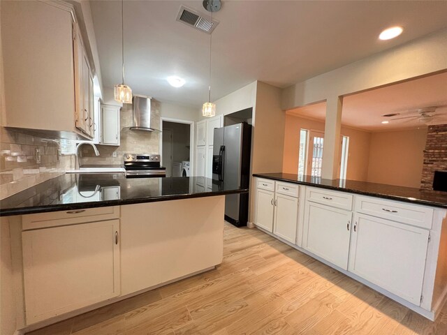 kitchen with light wood-style flooring, stainless steel appliances, a peninsula, visible vents, and wall chimney exhaust hood