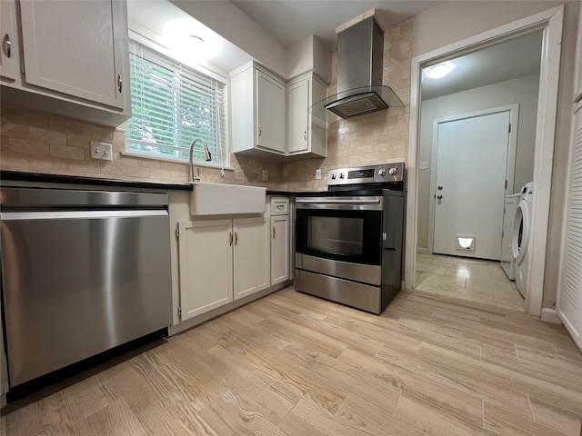 kitchen with tasteful backsplash, wall chimney exhaust hood, appliances with stainless steel finishes, light wood-style floors, and a sink