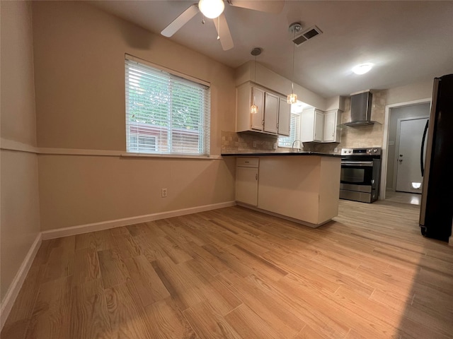 kitchen featuring dark countertops, wall chimney exhaust hood, freestanding refrigerator, a peninsula, and stainless steel electric stove