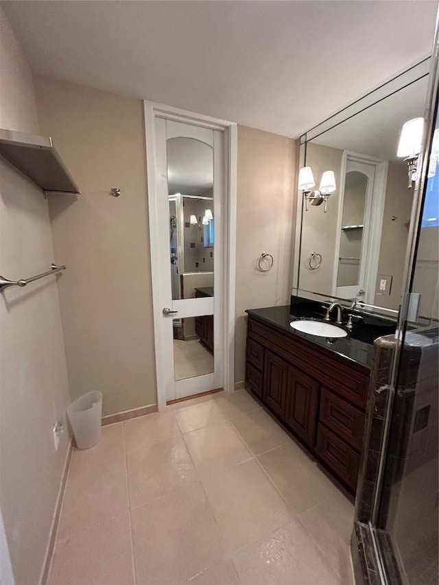 bathroom with a shower with door, vanity, baseboards, and tile patterned floors