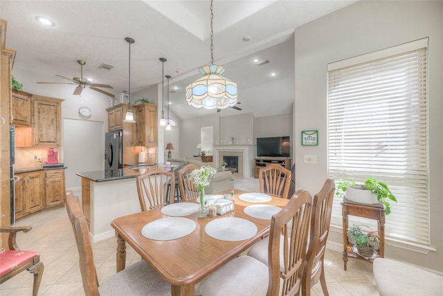 dining room with light tile patterned floors, lofted ceiling, a fireplace, visible vents, and a ceiling fan