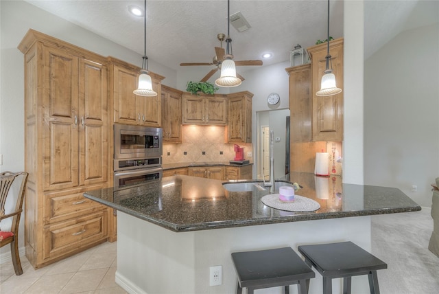 kitchen with a peninsula, appliances with stainless steel finishes, decorative backsplash, dark stone countertops, and pendant lighting