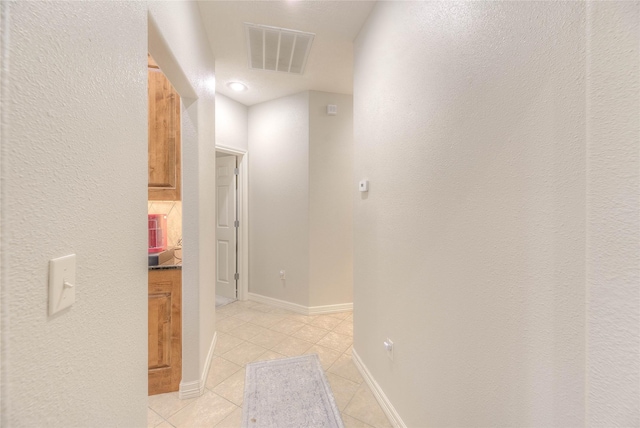 hallway with light tile patterned flooring, visible vents, and baseboards