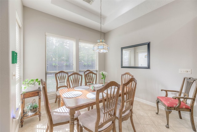 dining space with light tile patterned floors, a raised ceiling, and baseboards