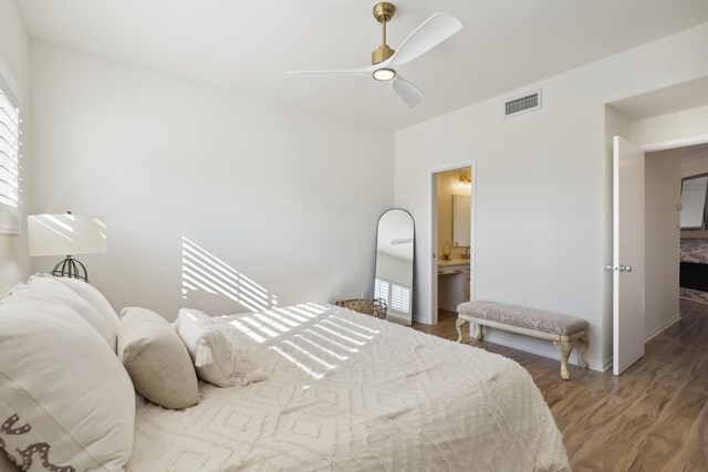 bedroom with connected bathroom, wood finished floors, visible vents, and a ceiling fan